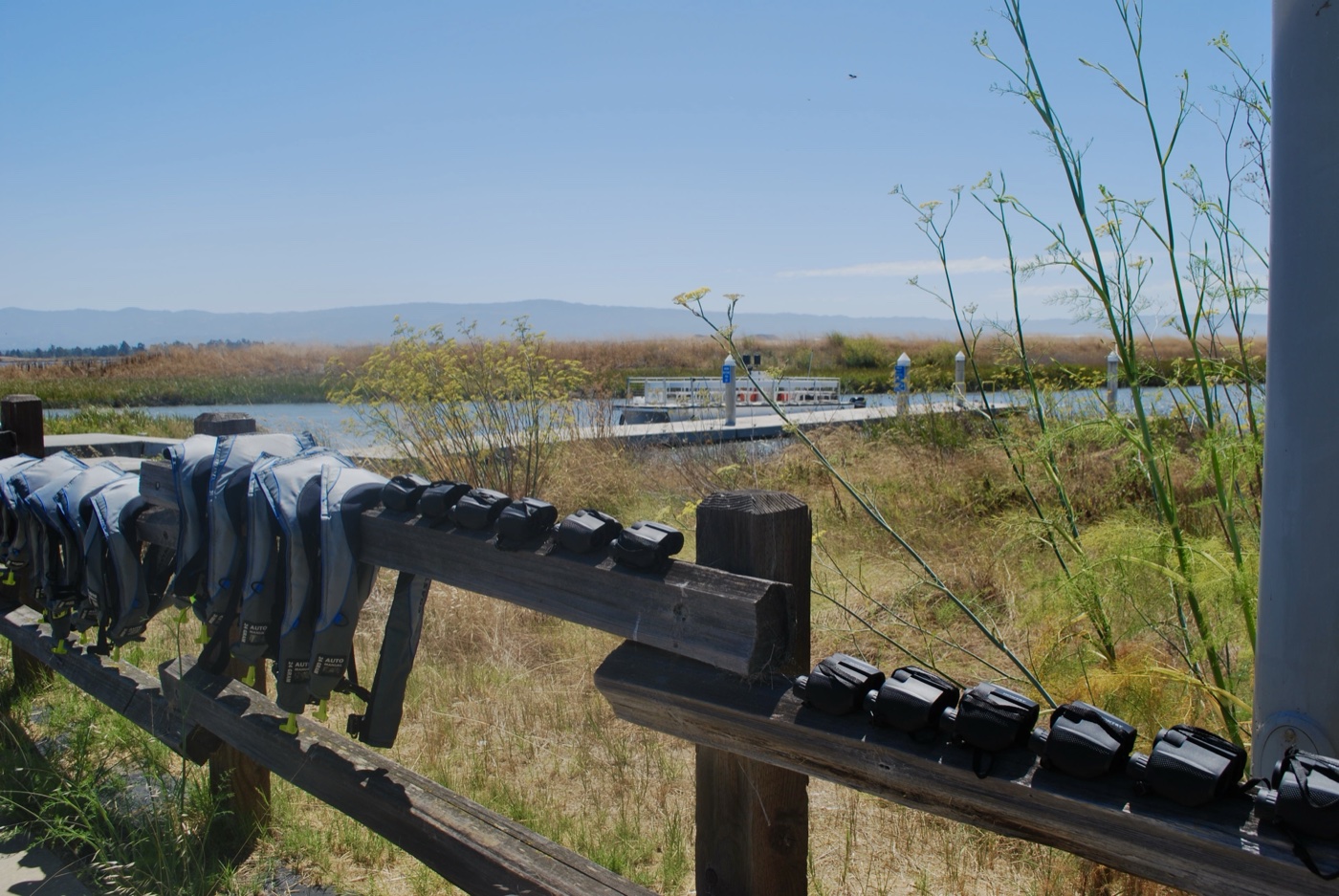 Wetlands with a boat dock in the distance and life vests hanging on a wooden fence
