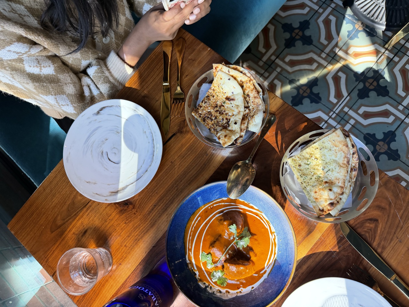 Overhead view of butter chicken and garlic naan on a wooden table with patterned tile floor