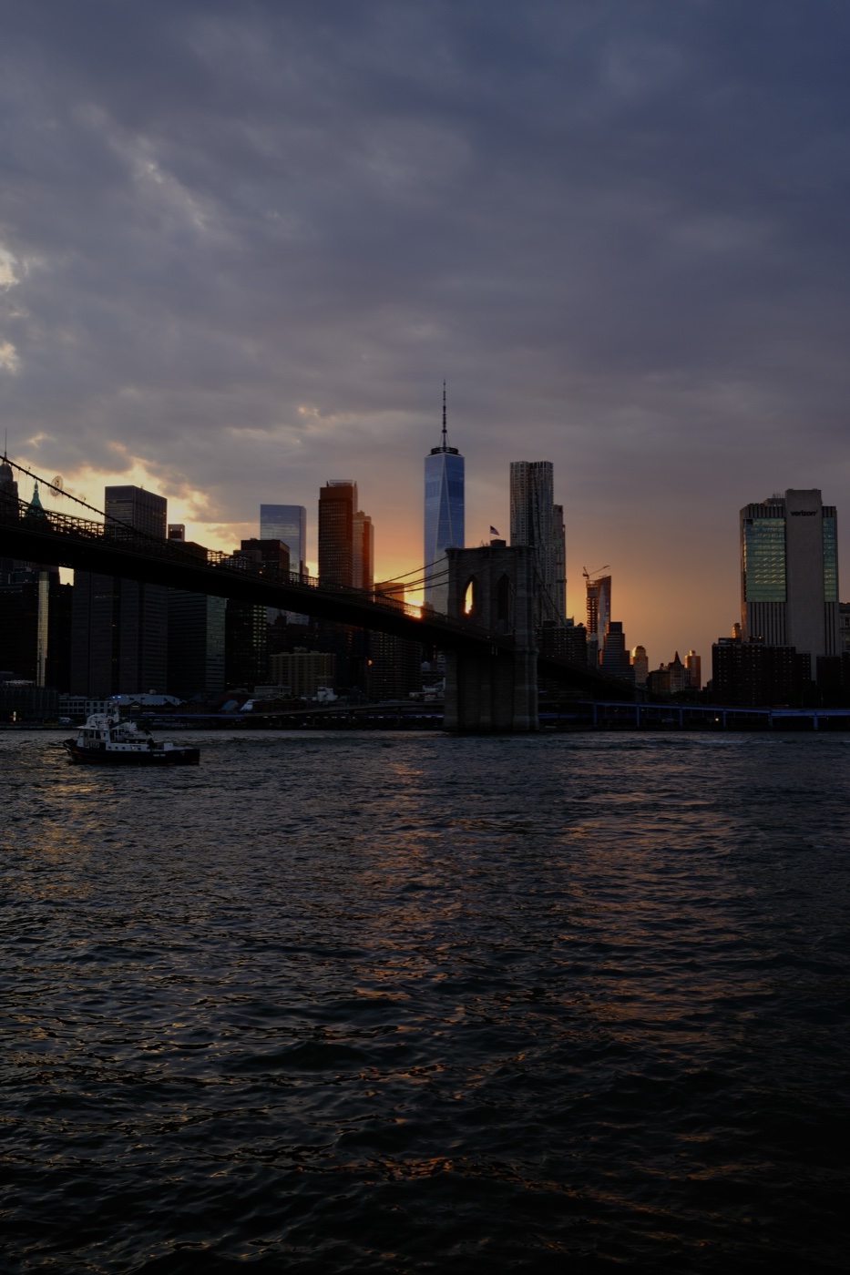 Manhattan skyline and Brooklyn Bridge at sunset with a small boat on the East River