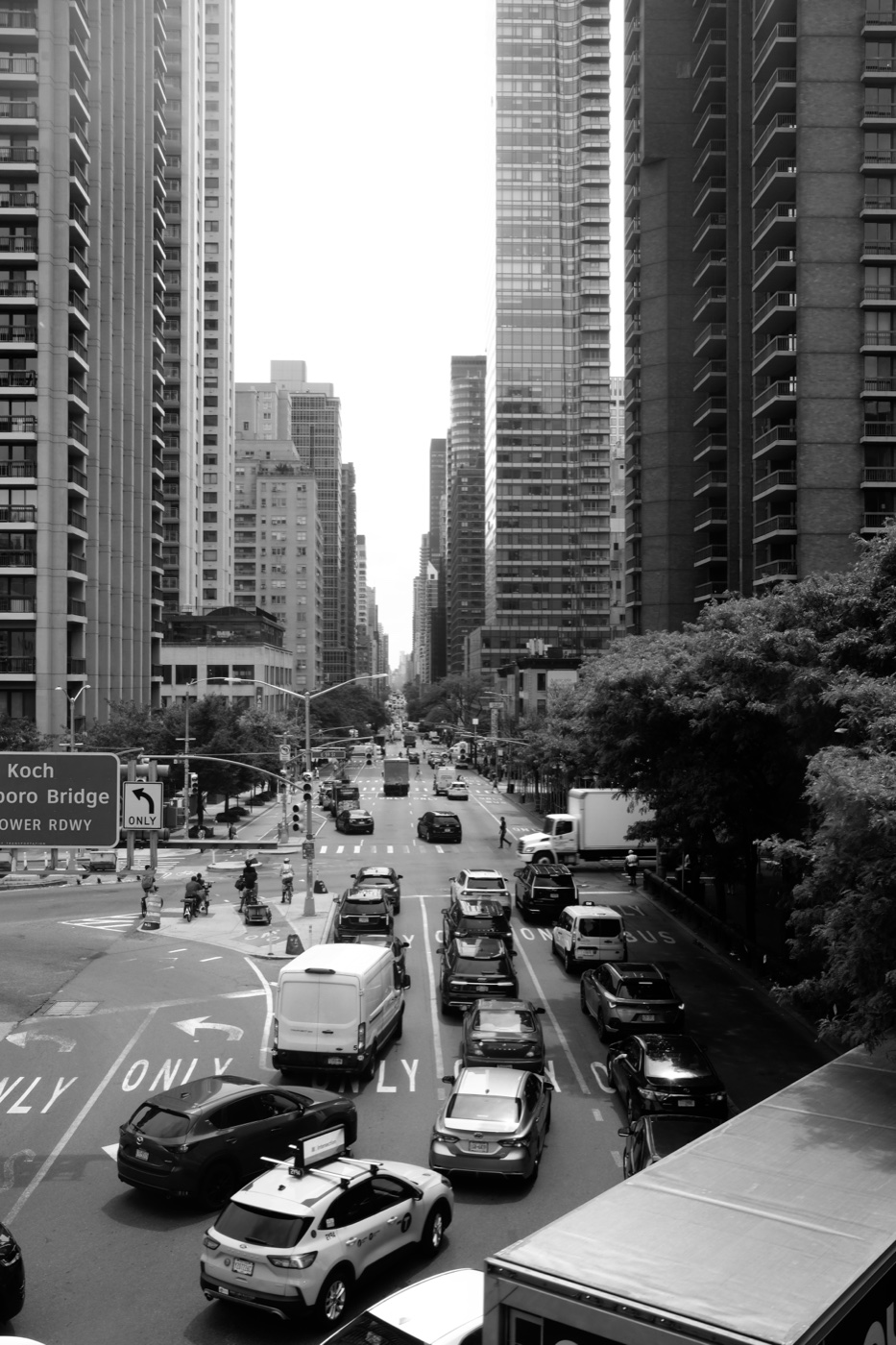 Black and white view of a Manhattan avenue with cars at an intersection between high-rise buildings